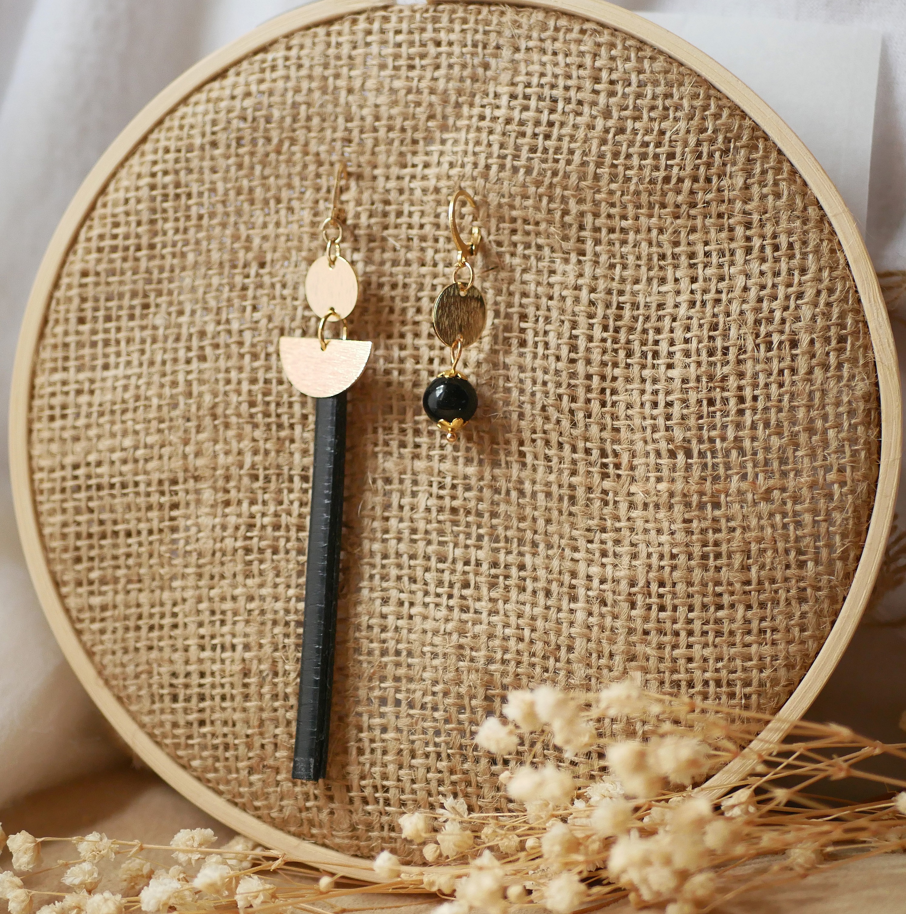 Boucle d'oreille pendante dorée avec tige en cuir noir.