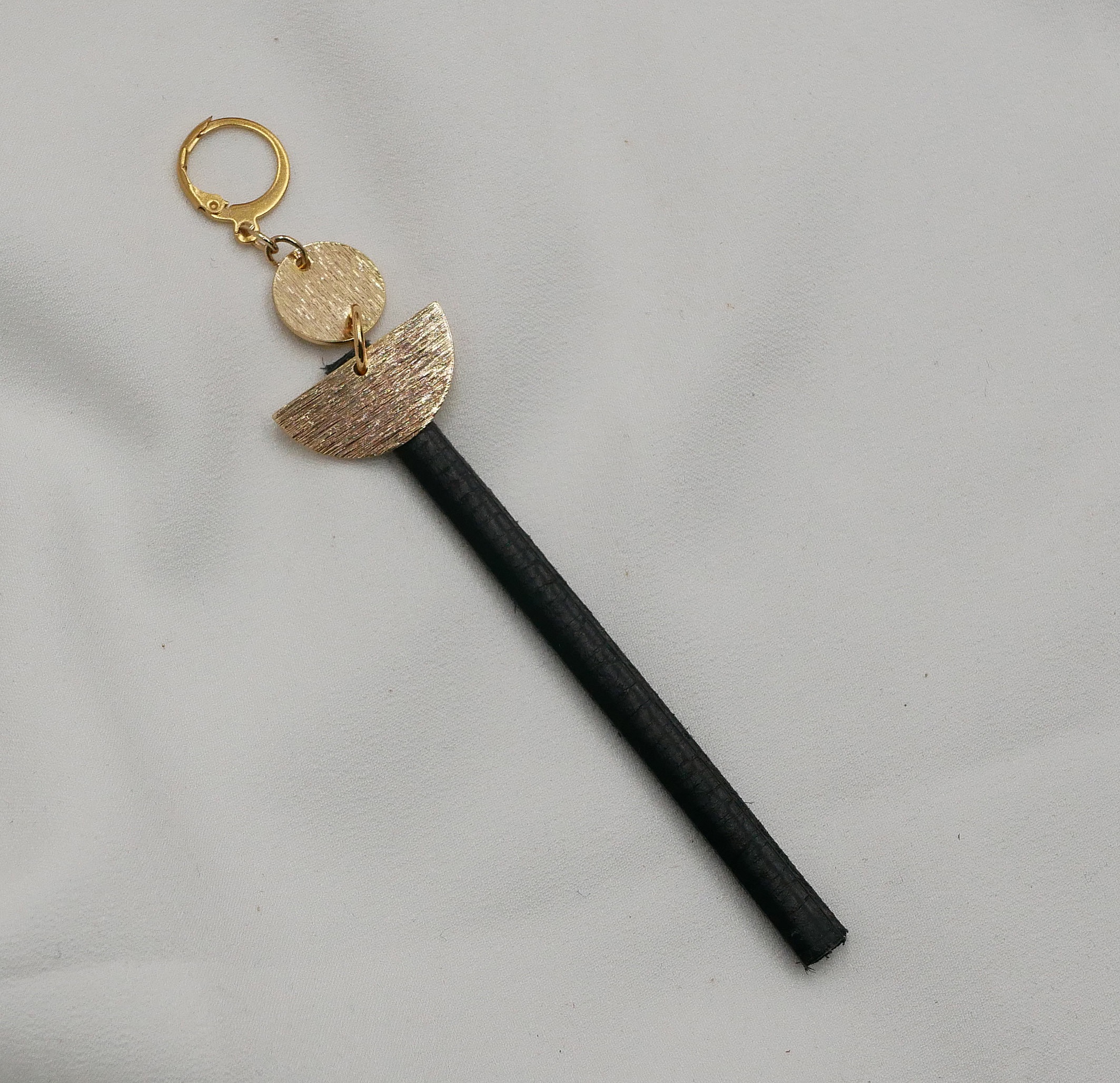 Boucle d'oreille pendante dorée avec tige en cuir noir.