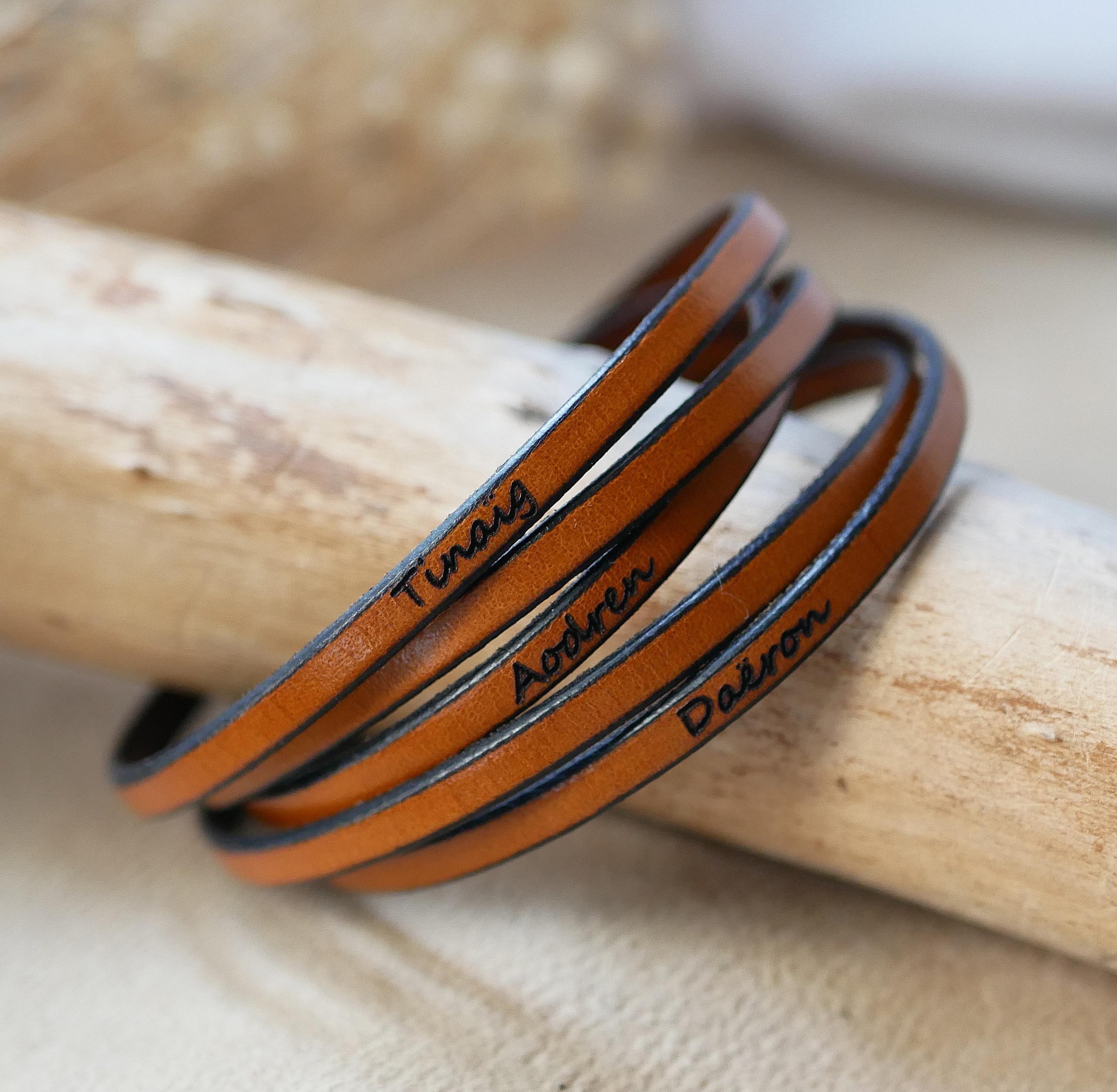 Bracelet fin en cuir marron gravé de prénoms personnalisés.