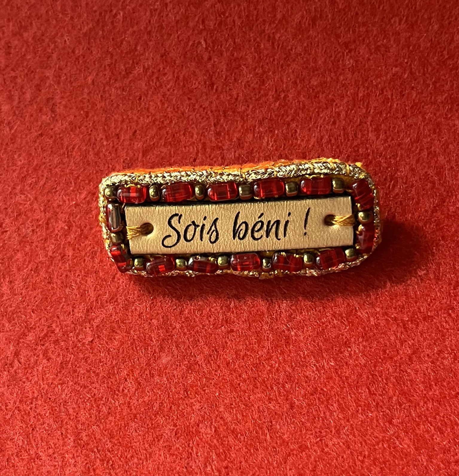 Broche à message en cuir gravé "sois béni" en perles rouges et dorées 