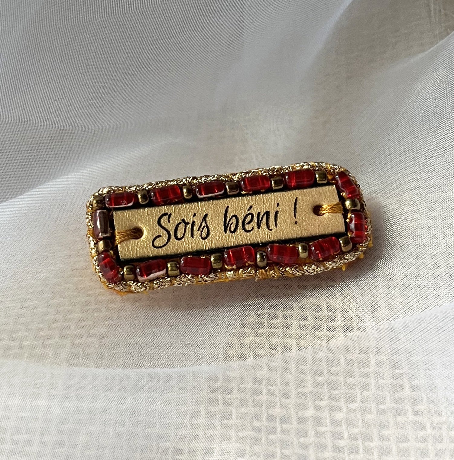 Broche &agrave; message en cuir grav&eacute; "sois b&eacute;ni" en perles rouges et dor&eacute;es 