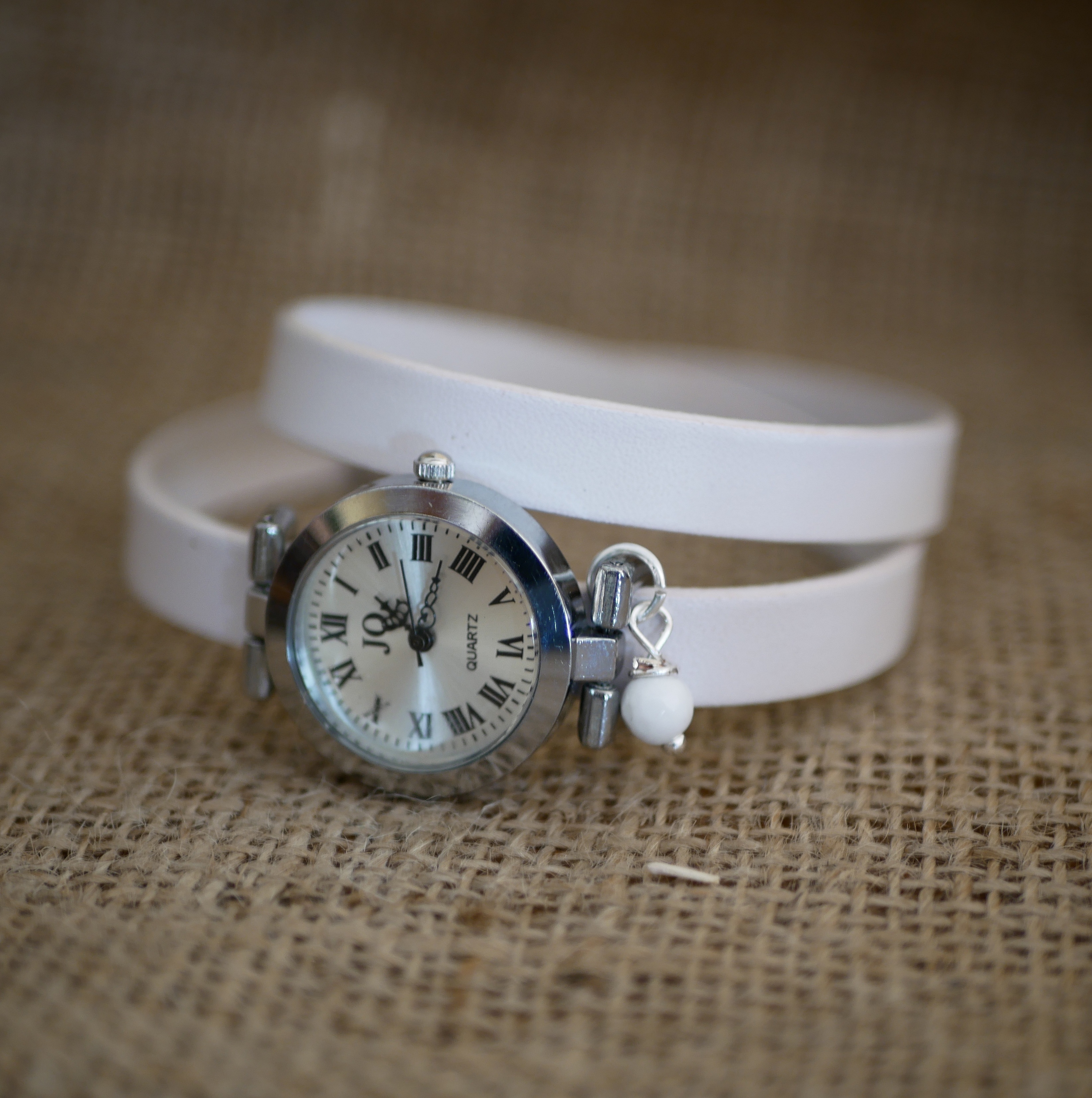 Montre argentée à cadran chiffres romains et bracelet blanc.